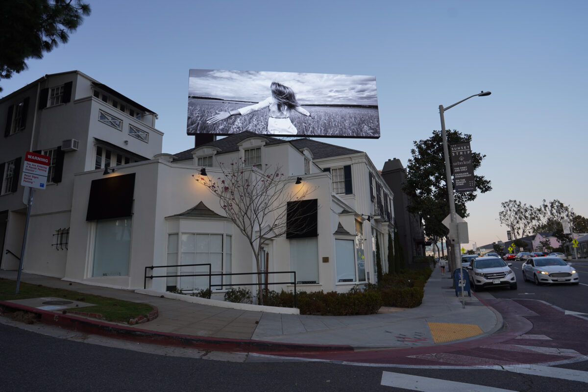 Glowing LED billboard on Sunset Blvd. West Hollywood displays artwork entitled "Reverse Women"by Sarah Rara. Images of running women advance backward and in slow motion as if the ground is being pulled out from under them.